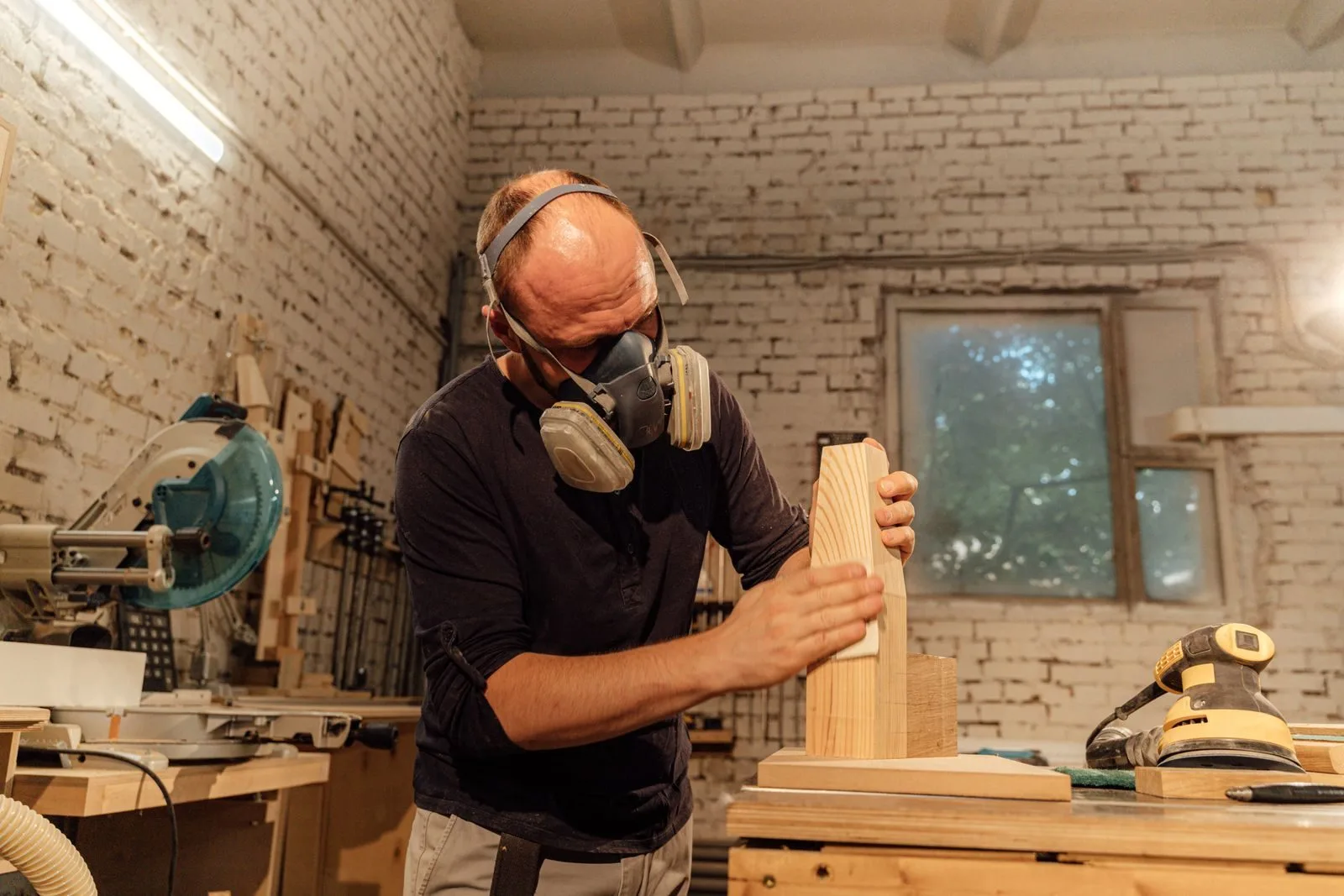 Agentes Nocivos para Aposentadoria Especial em 2026 1 A skilled carpenter wearing a respirator mask sands a wooden piece in his workshop.
