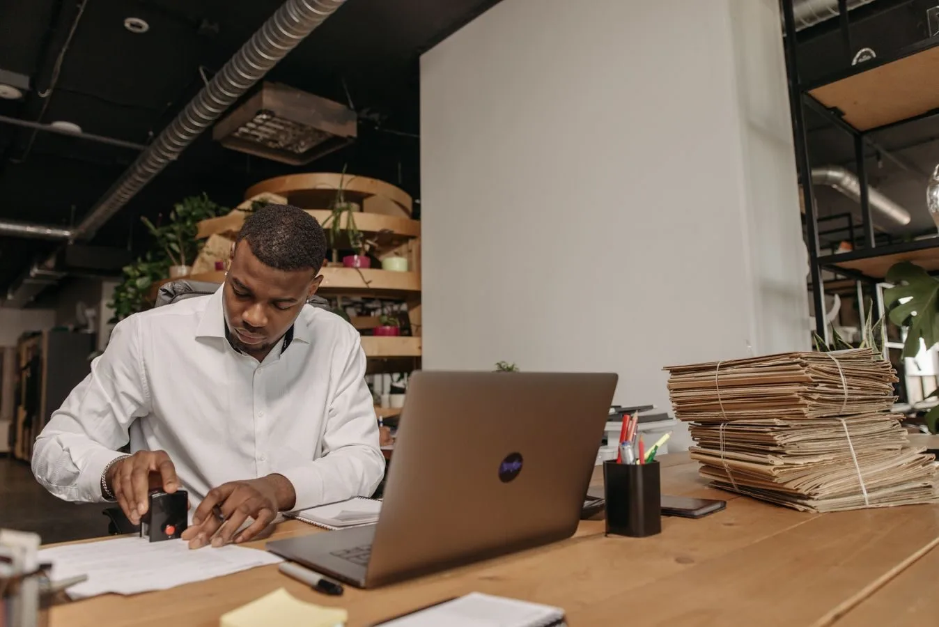 Anulação e revogação de atos: como o poder público desfaz suas próprias decisões 1 African American man focused on stamping documents at an office desk with a laptop and folders.