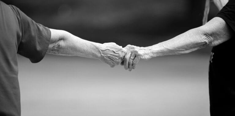 Como podemos ajudar? 8 Black and white photo of senior adults holding hands, symbolizing connection and love.