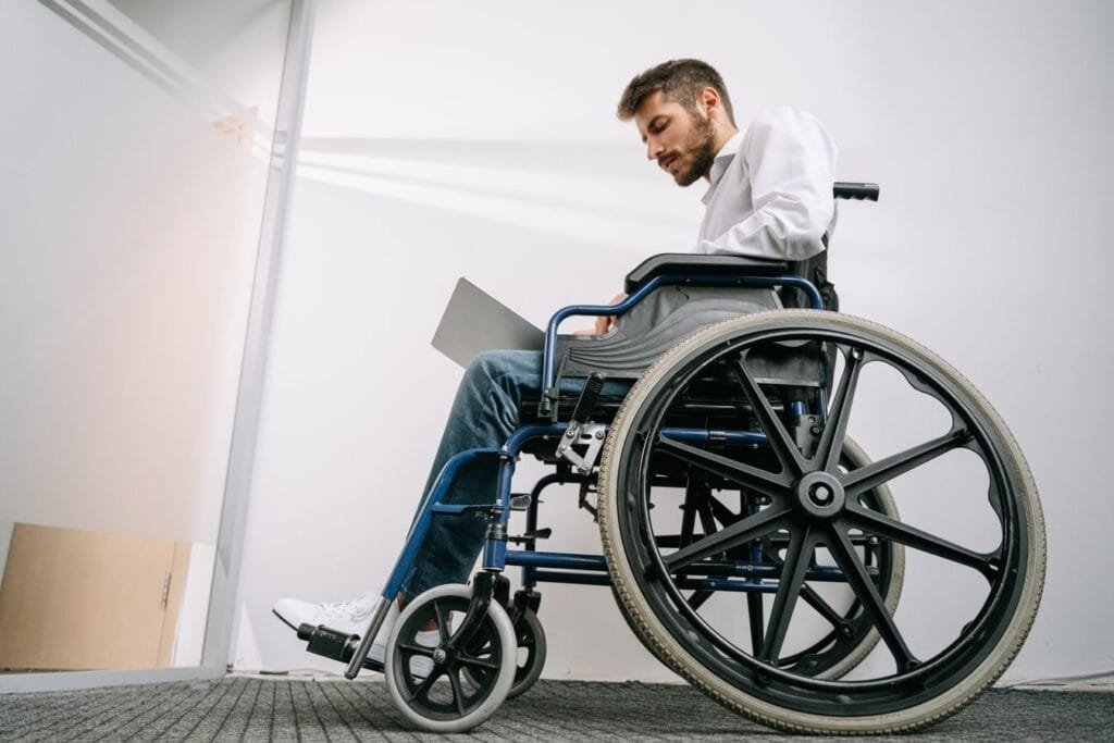 Sou pessoa com deficiência e trabalho. Posso me aposentar mais cedo? 1 A man in a wheelchair concentrates on work using a laptop in an office setting.