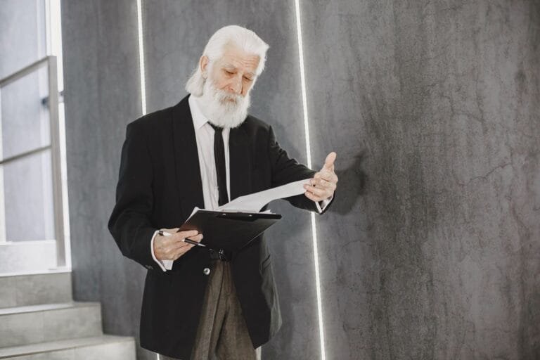 Senior man with white beard in suit reviewing documents indoors, in modern office setting.