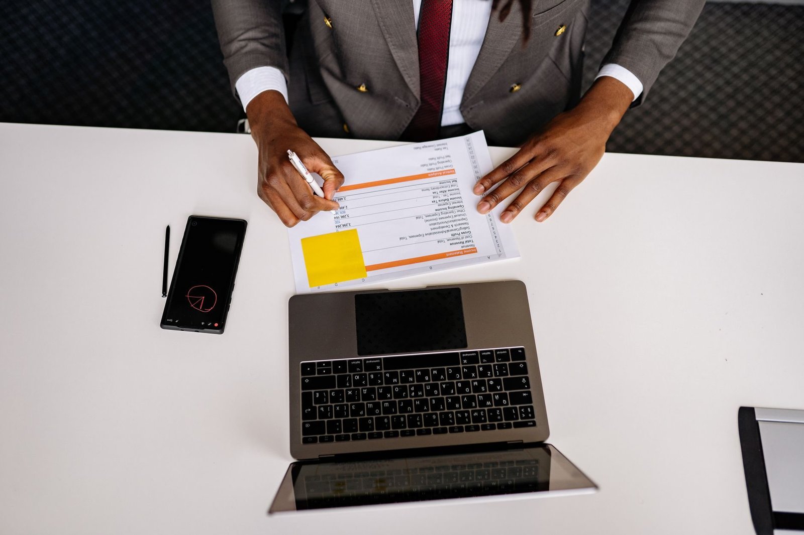 Top view of a business professional analyzing documents with a laptop on a white desk in a
