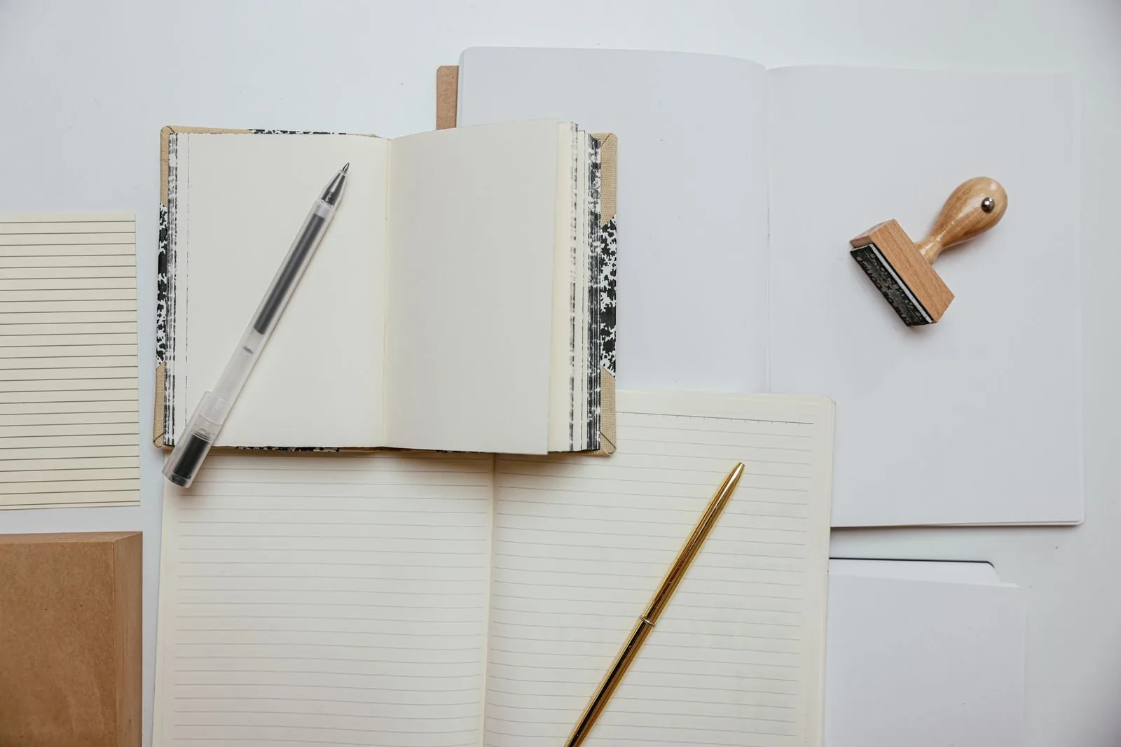 Flat lay of stationery items including notepads, pens, and a stamp on a white background.