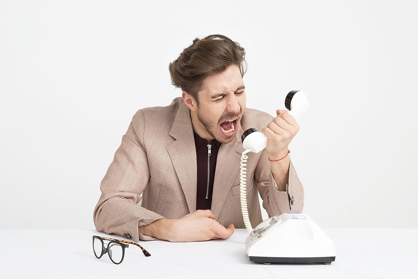 Avaliações negativas online: ofensa, crítica lícita ou difamação 1 Businessman in a beige suit shouting into a vintage telephone, expressing frustration at work.