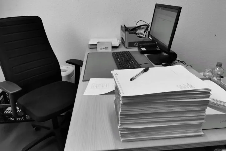 Banalização da perícia judicial médica: efeito colateral do Tema 125 do TST 4 Black and white image of a cluttered office desk with a computer, chair, and paperwork.