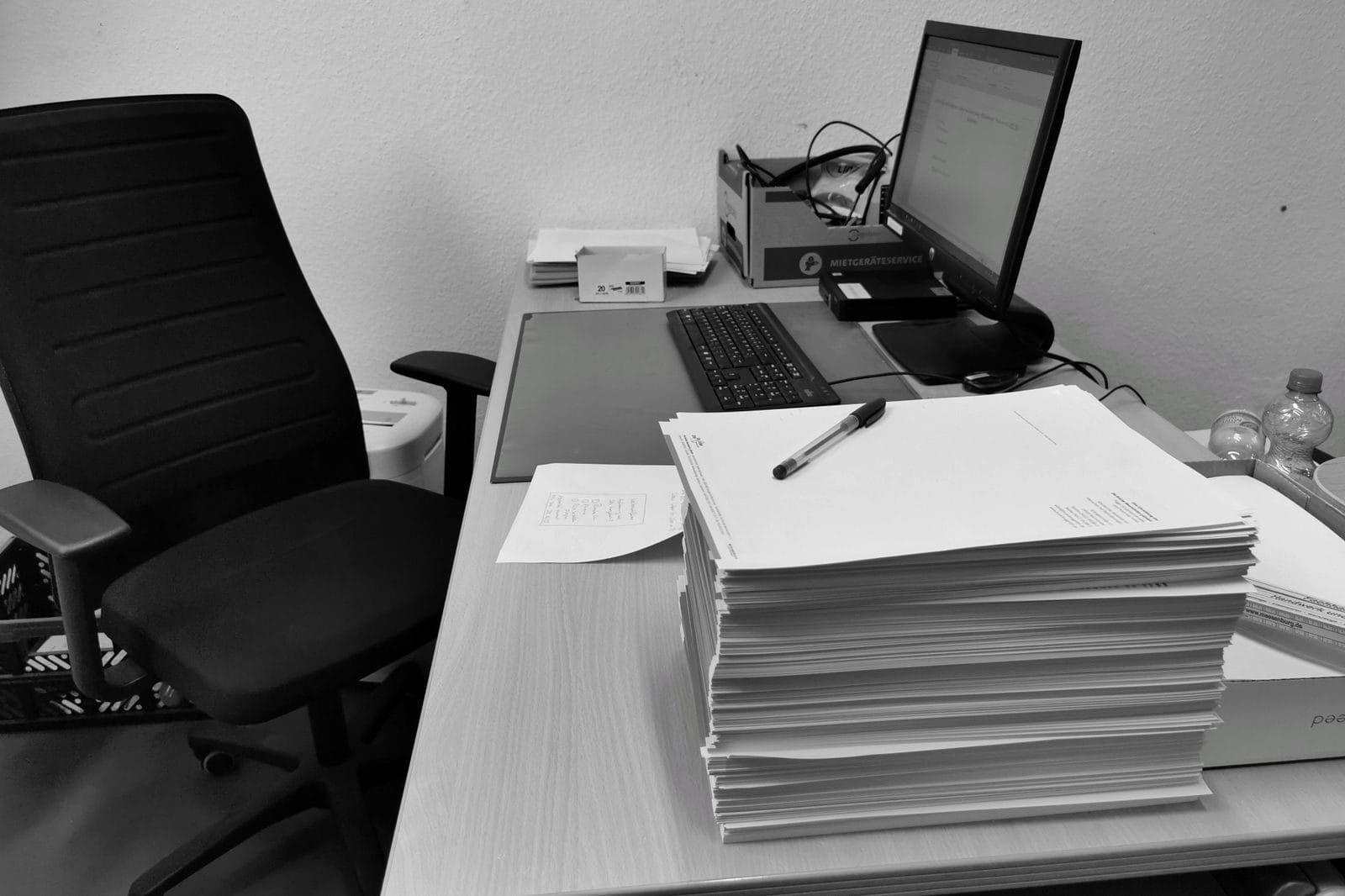 Banalização da perícia judicial médica: efeito colateral do Tema 125 do TST 1 Black and white image of a cluttered office desk with a computer, chair, and paperwork.