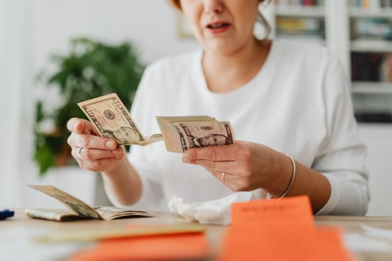 BPC/LOAS segue atrelado ao salário mínimo e passa a pagar R$ 1.621 em 2026, sem direito a 13º salário 5 A woman sits indoors counting cash at her office desk, focusing on finances.