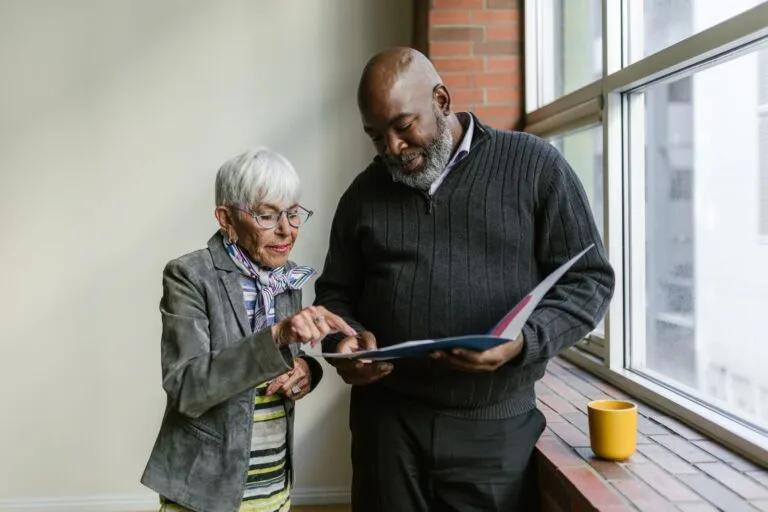 An elderly man and woman engage in a business discussion, reviewing documents in an office setting.