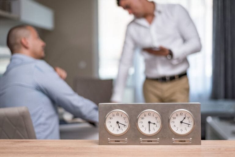 Cargo de confiança bancário e a jornada de seis horas da CLT 4 Two businessmen in an office with clocks displaying Dubai, Sofia, London time.