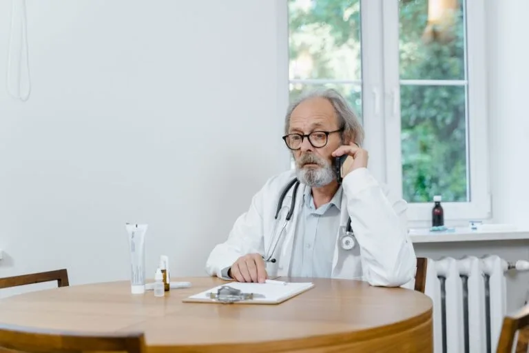 A senior doctor making a telemedicine call in an office setting, discussing medical cases.