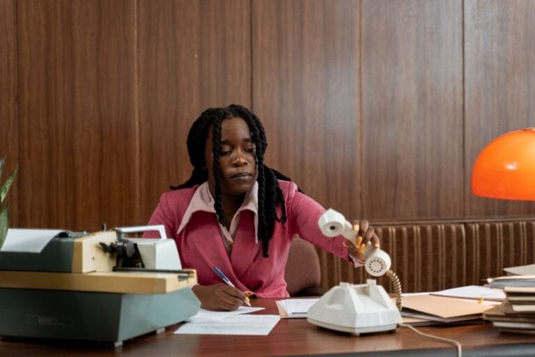 An adult woman in a vintage office setting, handling a rotary phone.