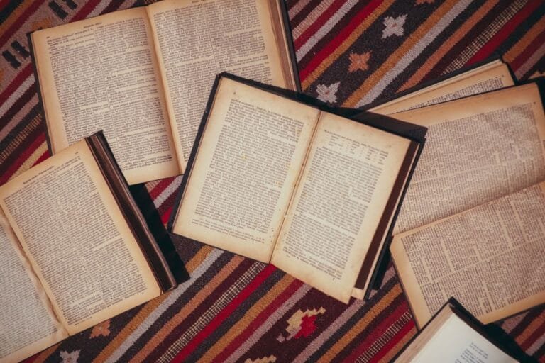 Resultados 7 Several vintage open books arranged on a colorful patterned rug in a flat lay style.