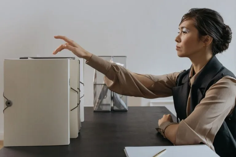 CNIS Errado: Como Corrigir Vínculos no INSS em 2026 5 Asian woman efficiently organizing documents at an office desk.