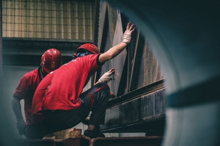 Cobrança de metas fora do expediente e o direito à desconexão 3 Two workers in red helmets assembling metal components inside a factory.