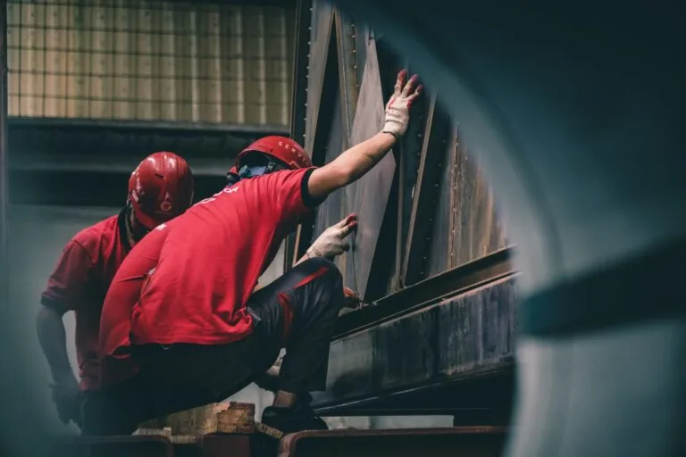 Cobrança de metas fora do expediente e o direito à desconexão 6 Two workers in red helmets assembling metal components inside a factory.