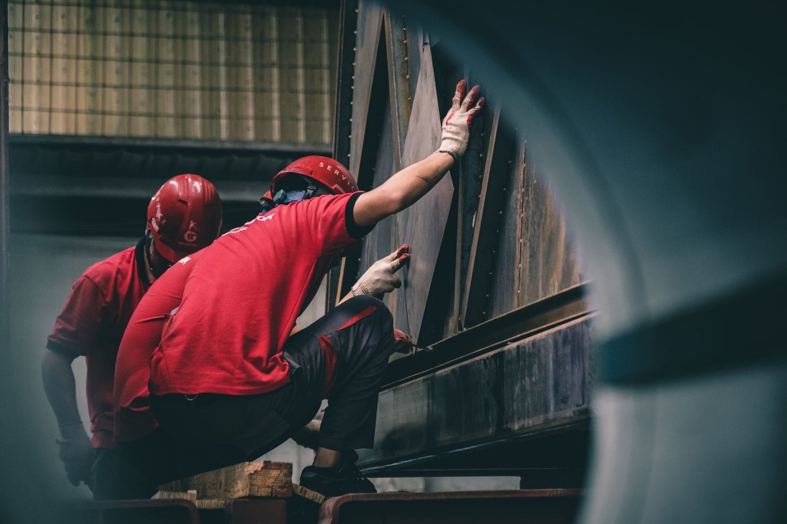 Cobrança de metas fora do expediente e o direito à desconexão 1 Two workers in red helmets assembling metal components inside a factory.