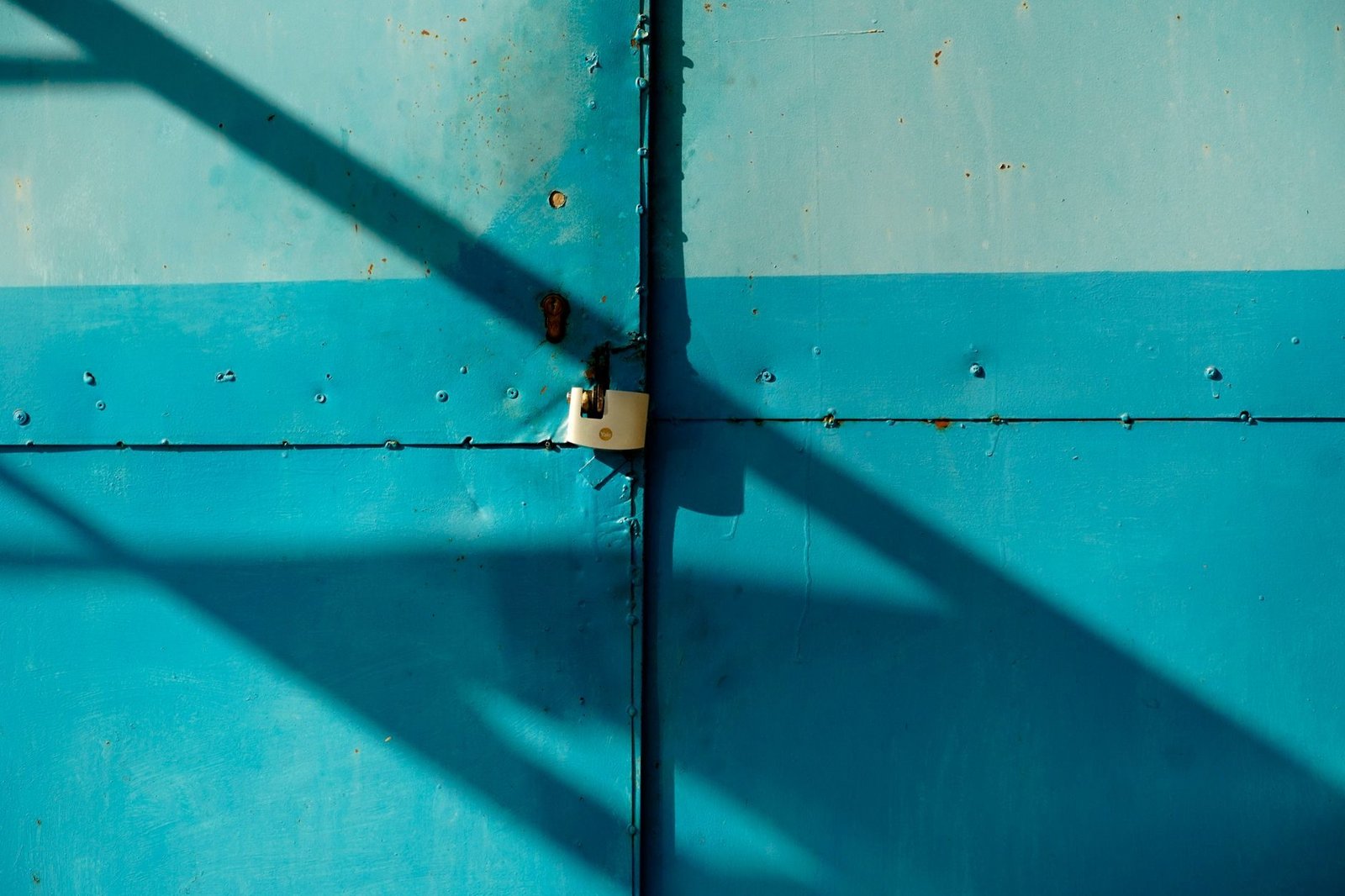 Cobranca e negativacao indevida a partir de dados vazados: como reagir 1 A close-up of a blue metal door secured with a padlock, casting shadows in the sunlight.