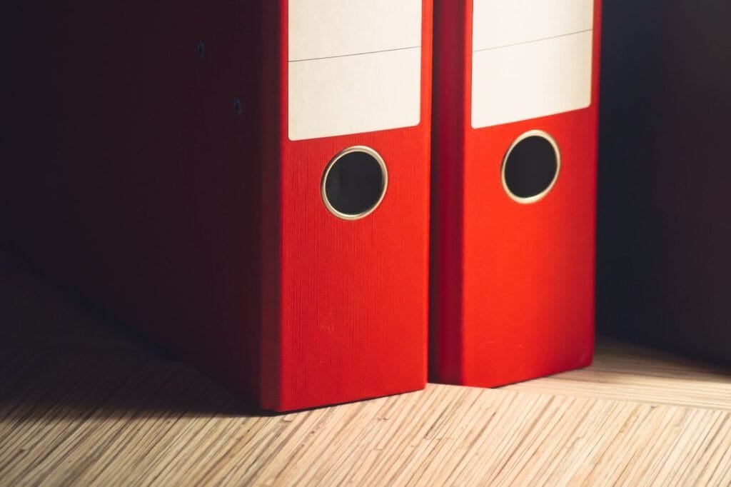 Como contestar desconto de consignado indevido no benefício 1 Close-up of two red lever arch files on a wooden desk in a modern office setting.