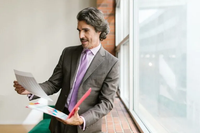 Como escolher entre sociedade limitada e empresa individual ao abrir um negócio 6 Businessman in a gray suit reviewing paperwork by a large window in an office setting.