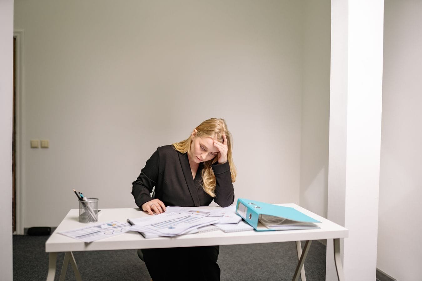 Como o bancário reúne provas do assédio moral por metas 1 A stressed businesswoman reviewing documents at her desk, overwhelmed by paperwork.