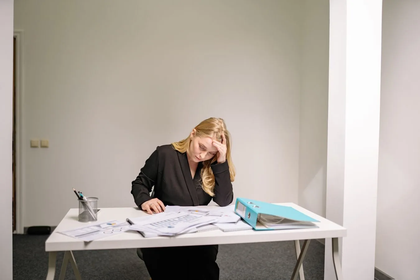 Como o bancário reúne provas do assédio moral por metas 1 A stressed businesswoman reviewing documents at her desk, overwhelmed by paperwork.