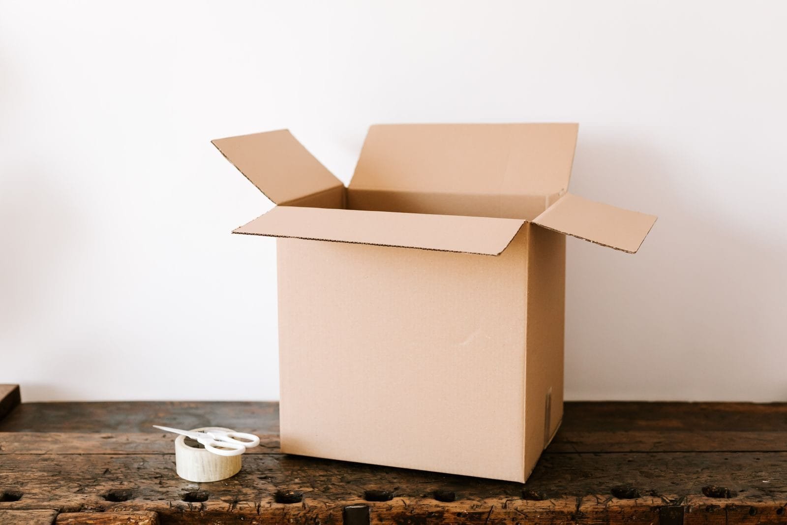 Compras em marketplace: quem responde quando o produto não chega ou vem com defeito 1 Opened cardboard container placed on old wooden desk near tape and scissors before relocation against white wall