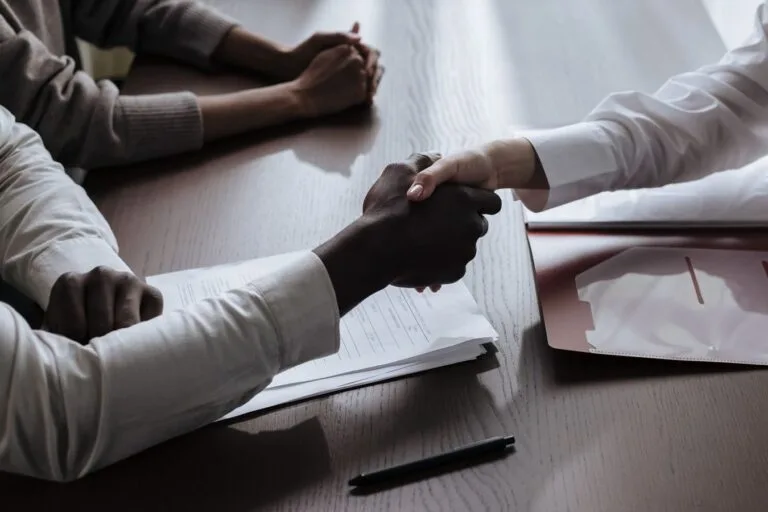 Business agreement with a handshake over contract documents at a meeting table.