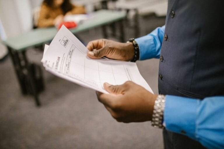Como podemos ajudar? 5 An instructor examining test papers in a classroom setting, focusing on education and evaluation.