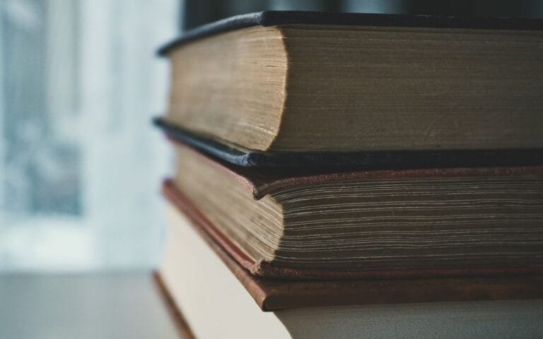 Resultados 4 A close-up view of a stack of vintage books with worn pages and covers in soft lighting.