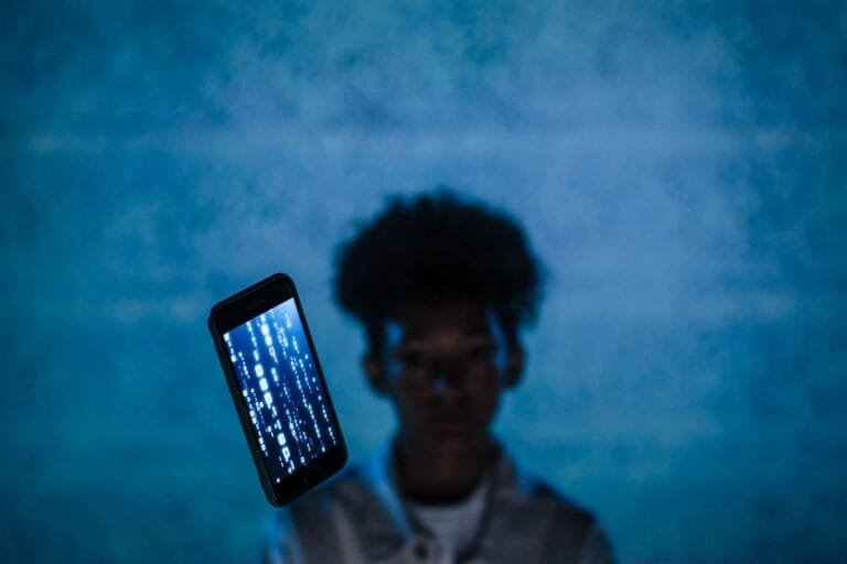 Conta falsa anuncia em meu nome: como combater o golpe que usa sua marca 5 A smartphone with digital code floats in focus, blurring the person behind, suggesting digital immersion.