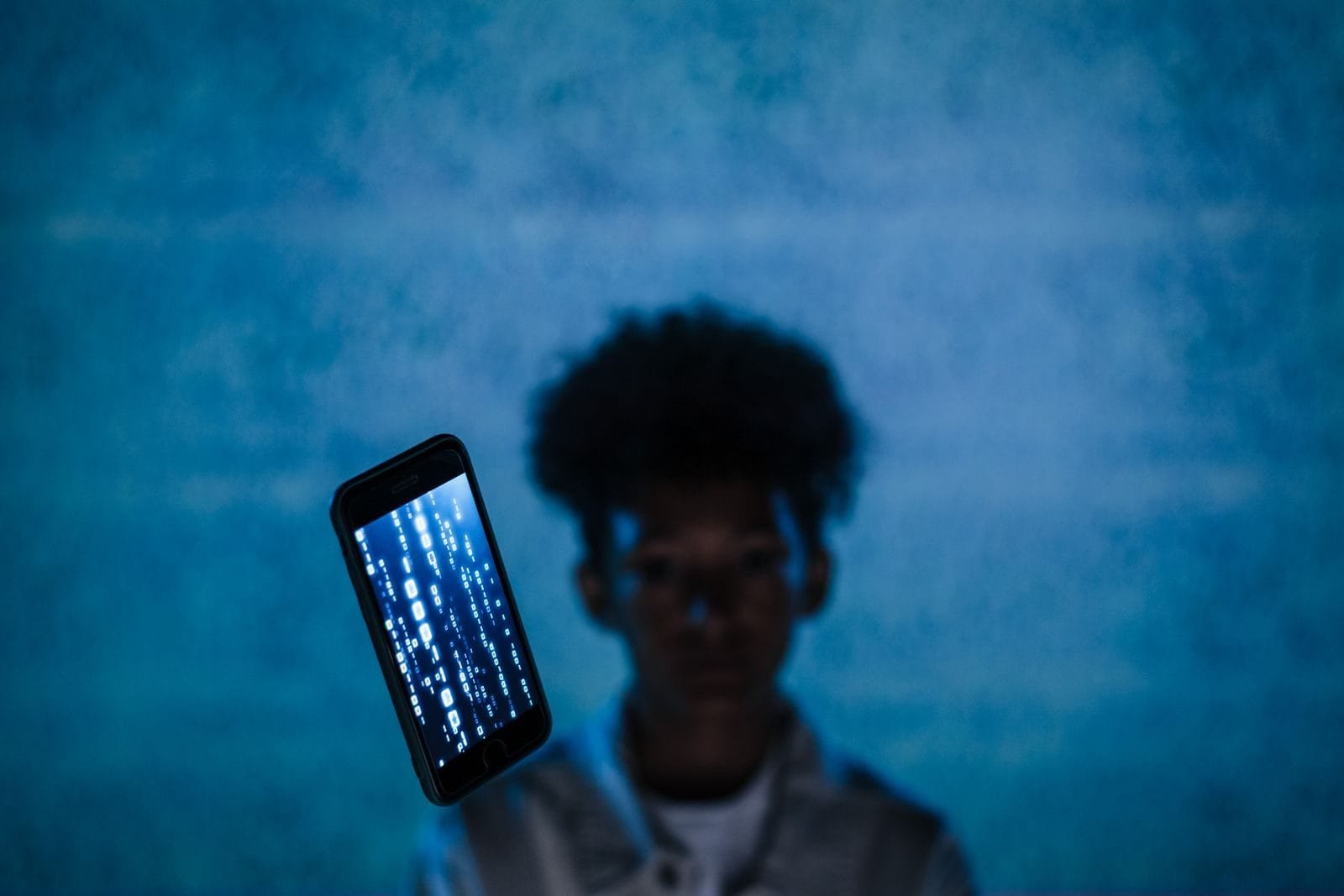 Conta falsa anuncia em meu nome: como combater o golpe que usa sua marca 1 A smartphone with digital code floats in focus, blurring the person behind, suggesting digital immersion.