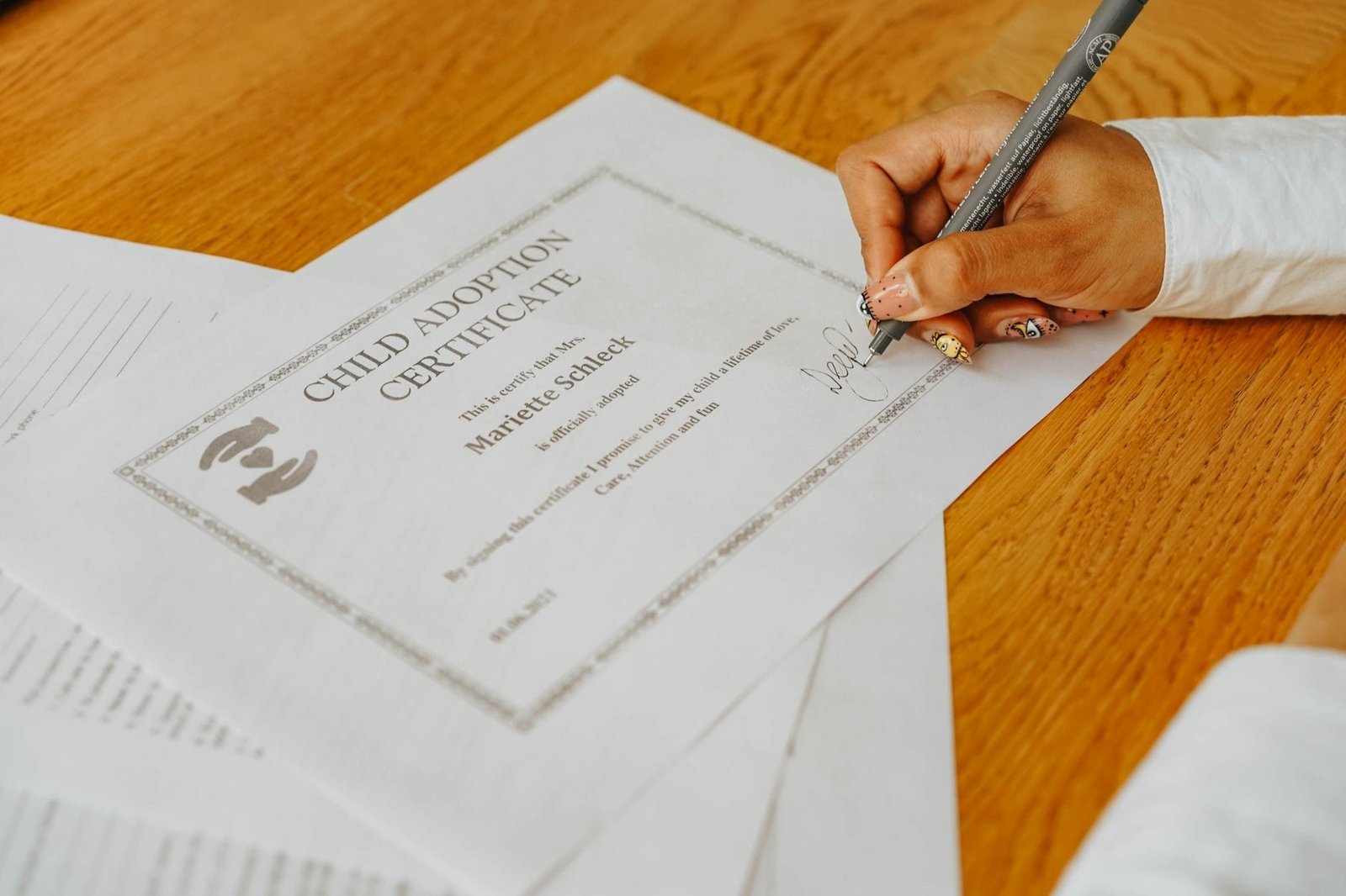 Contraditorio e ampla defesa fora do tribunal: o que significam na pratica 1 A close-up of a hand signing a child adoption certificate with a pen on a wooden table.