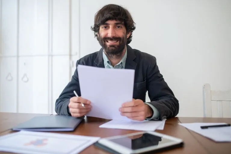 Contraditório e ampla defesa fora do tribunal: o que significam na prática 5 Smiling businessman in a black jacket reviewing documents at his desk, indoors.