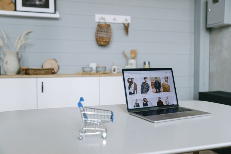 A laptop displaying an online shopping portal sits on a minimal desk with a miniature shop
