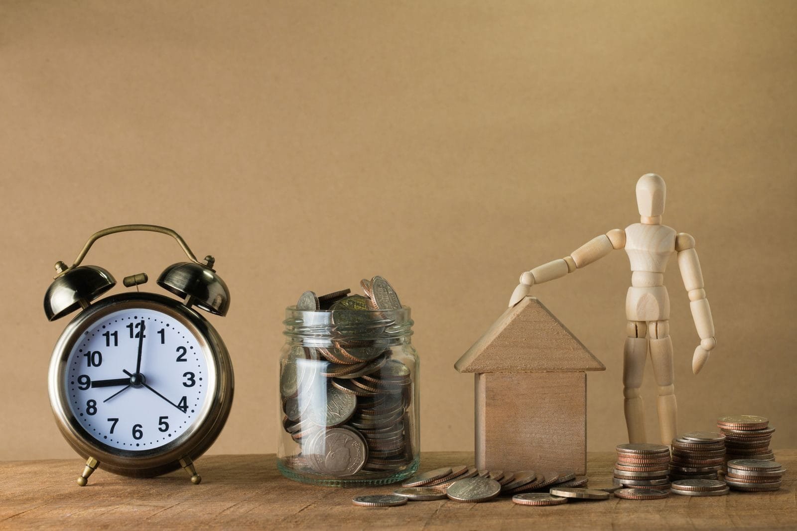 Contribuição Facultativa: Quem Pode Contribuir e Quais são as Vantagens 1 Wooden mannequin with a house, coins, and clock symbolizing time and financial planning.