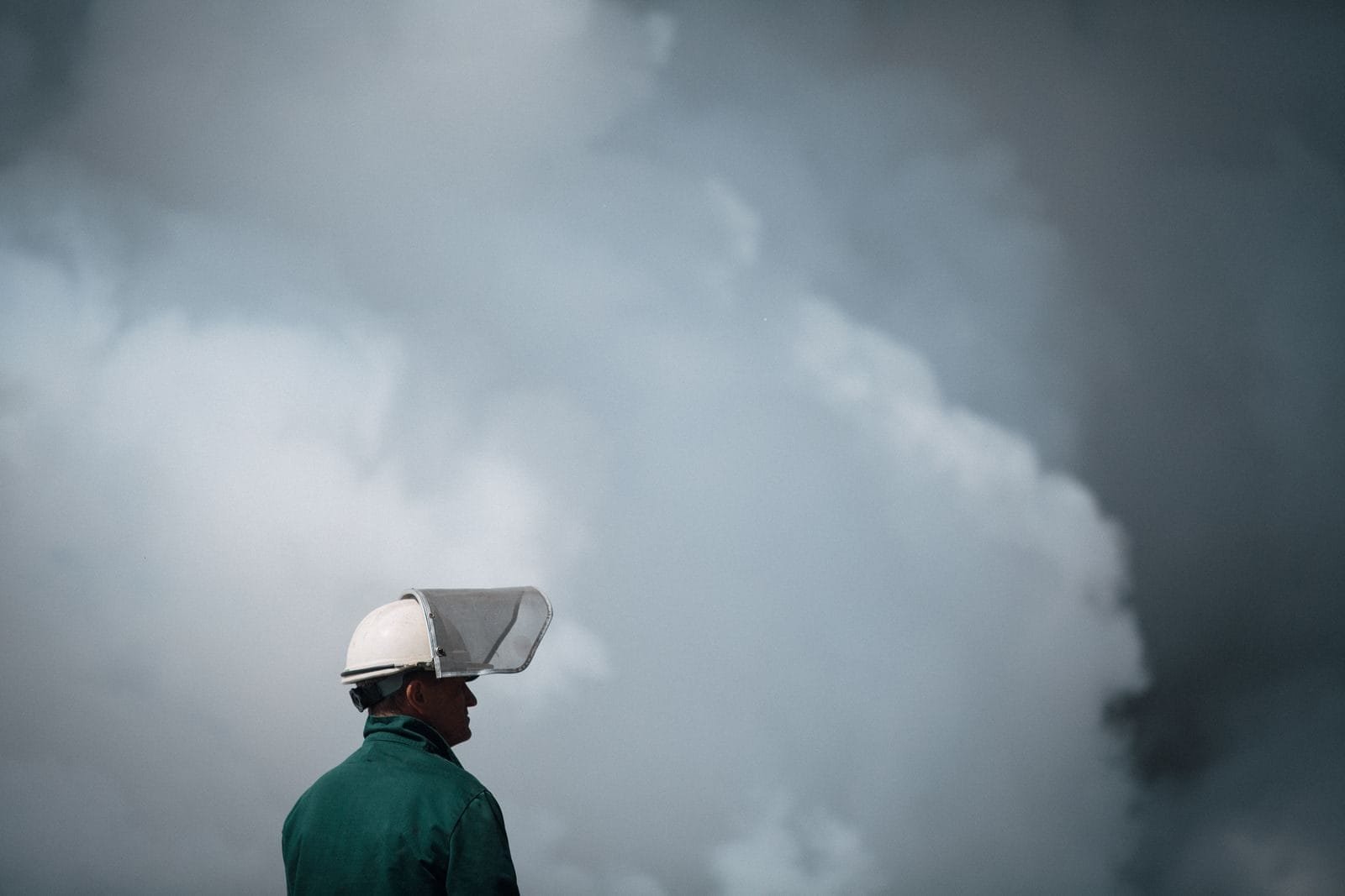 A worker in protective gear stands in front of thick smoke, highlighting industrial air pollution.