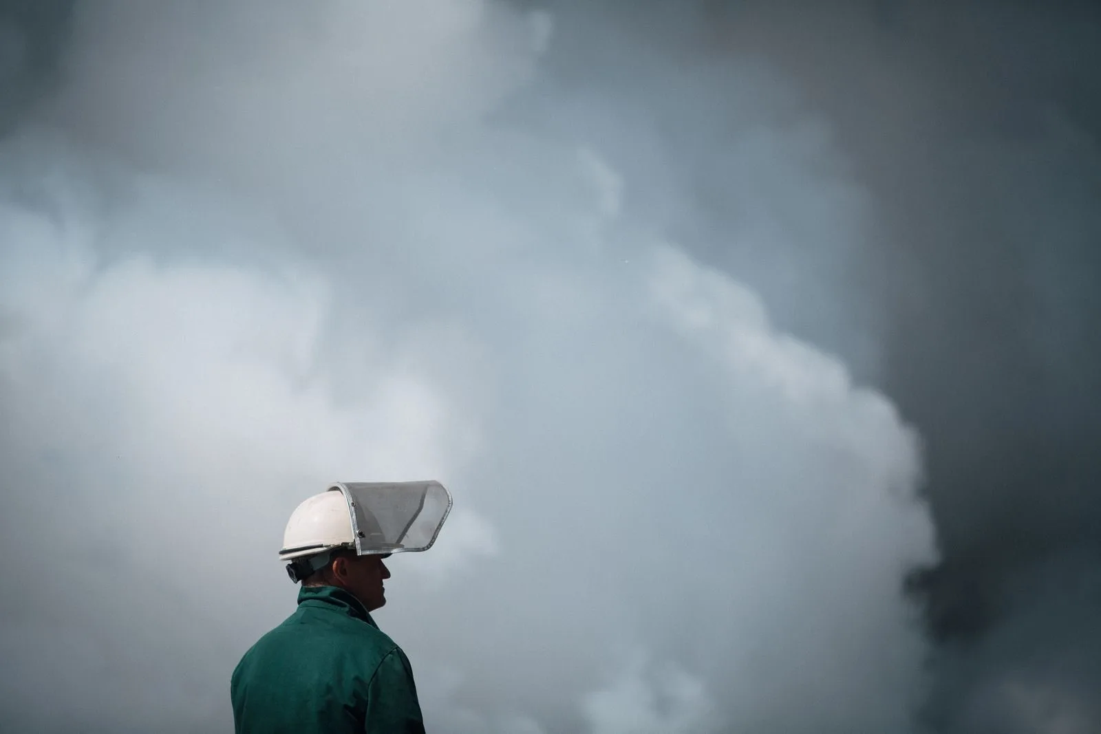 A worker in protective gear stands in front of thick smoke, highlighting industrial air pollution.