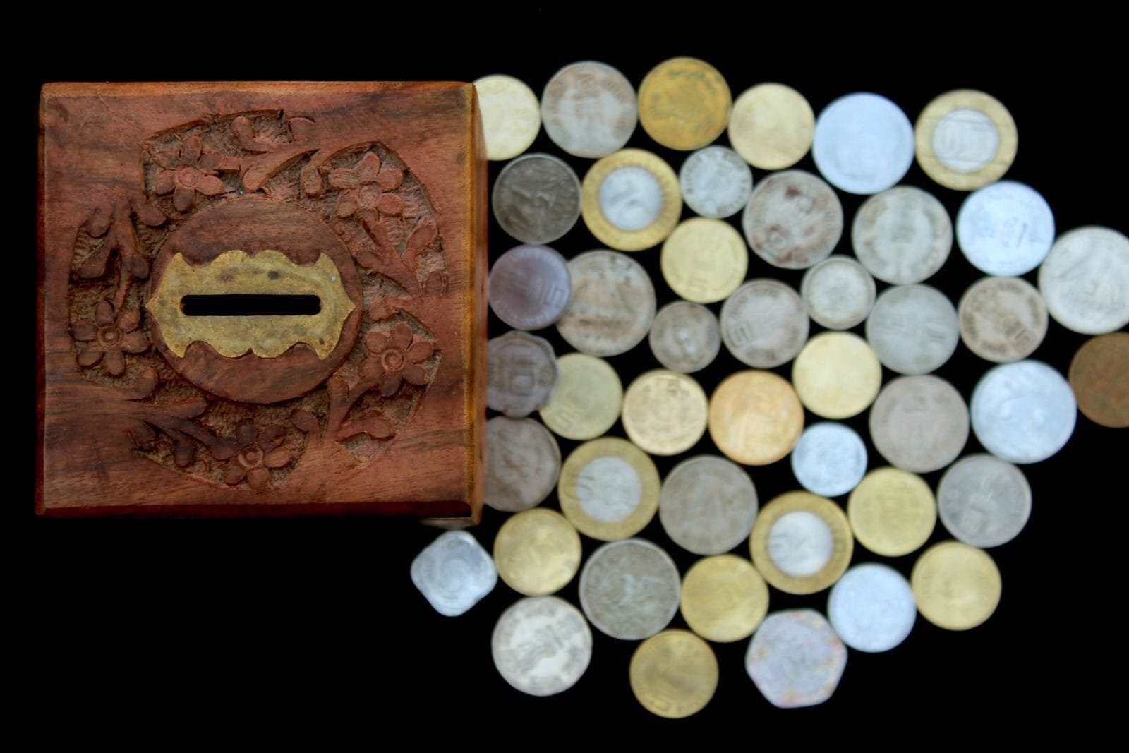 Crimes Eleitorais: Compra de Votos, Boca de Urna e Fake News 1 Top view of a vintage wooden piggy bank and assorted coins on a black surface, symbolizing savings and wealth.