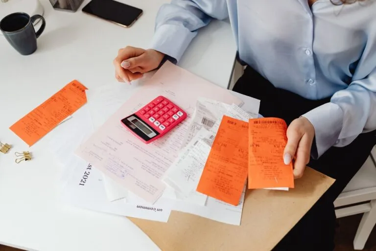 Custas, taxas e despesas: o verdadeiro custo de processar 8 A woman reviews receipts and calculates expenses at a desk with a pink calculator.