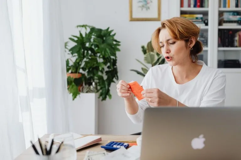 Dependência Econômica para Pensão por Morte em 2026 3 Woman reviewing bills at home desk with laptop and plants, managing personal finances.