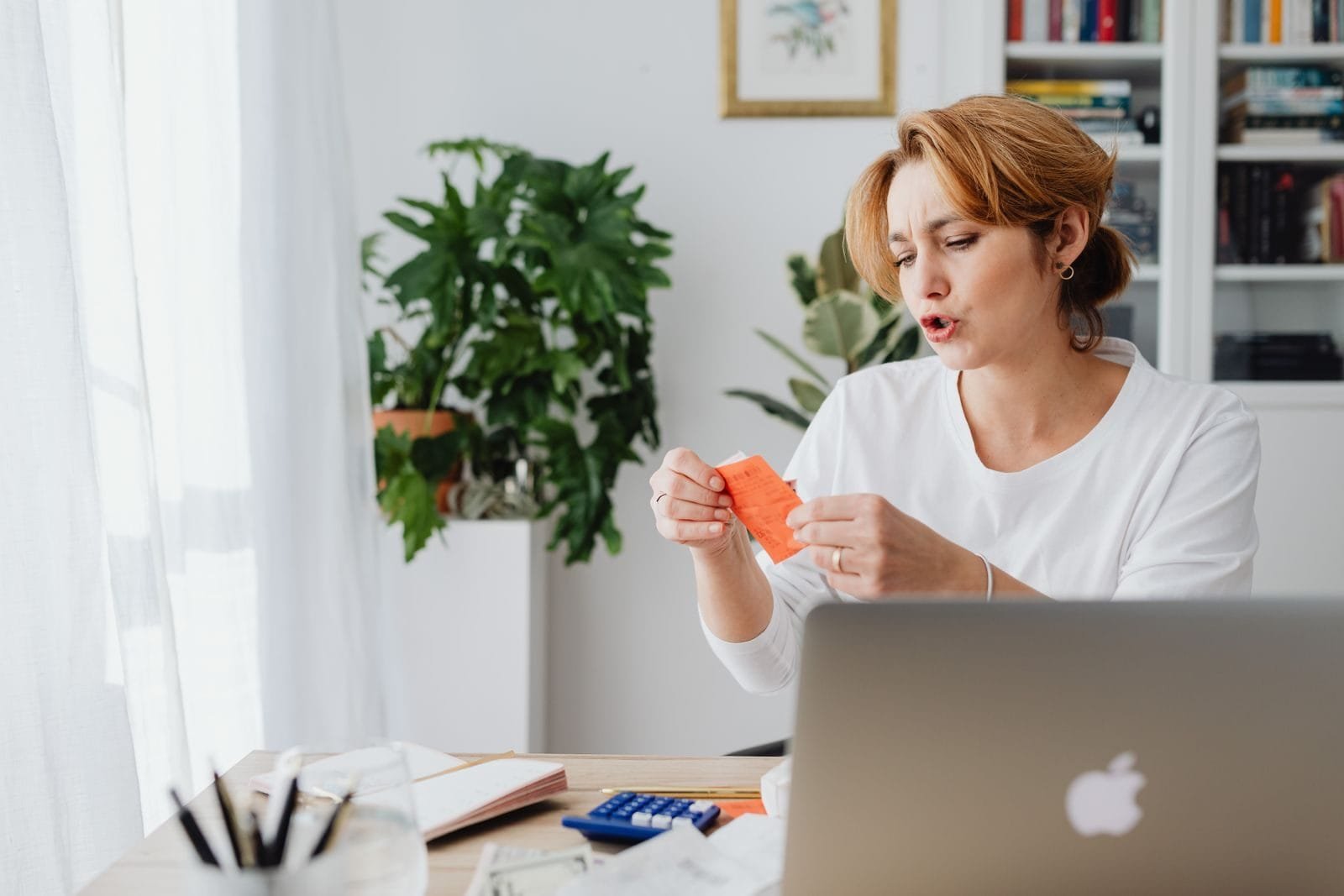 Dependência Econômica para Pensão por Morte em 2026 1 Woman reviewing bills at home desk with laptop and plants, managing personal finances.
