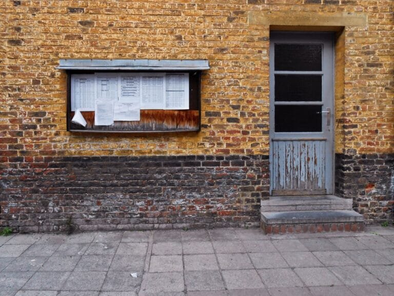 A rustic brick wall in Mons, Belgium, featuring a notice board and weathered door.