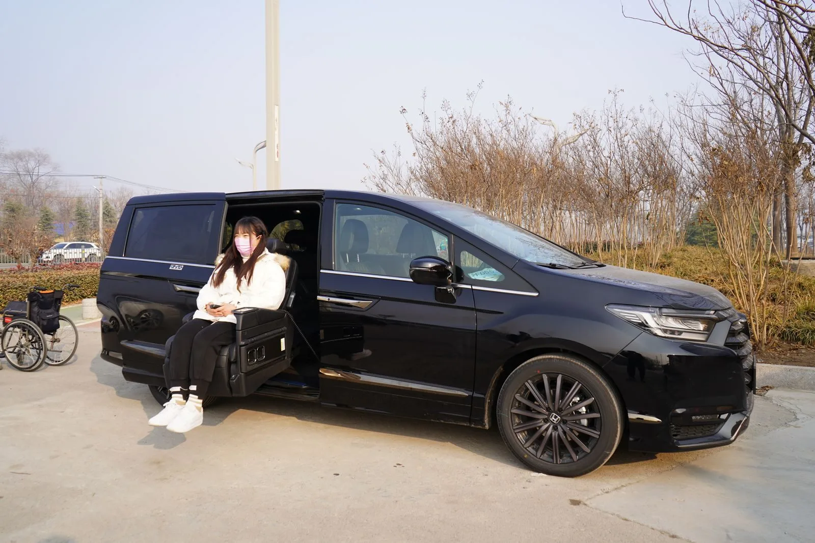 Woman in face mask using sliding seat in black car with nearby wheelchair.