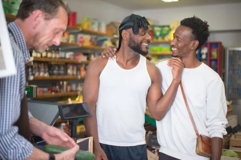 Two men share a friendly moment in a Portuguese grocery store with a clerk.
