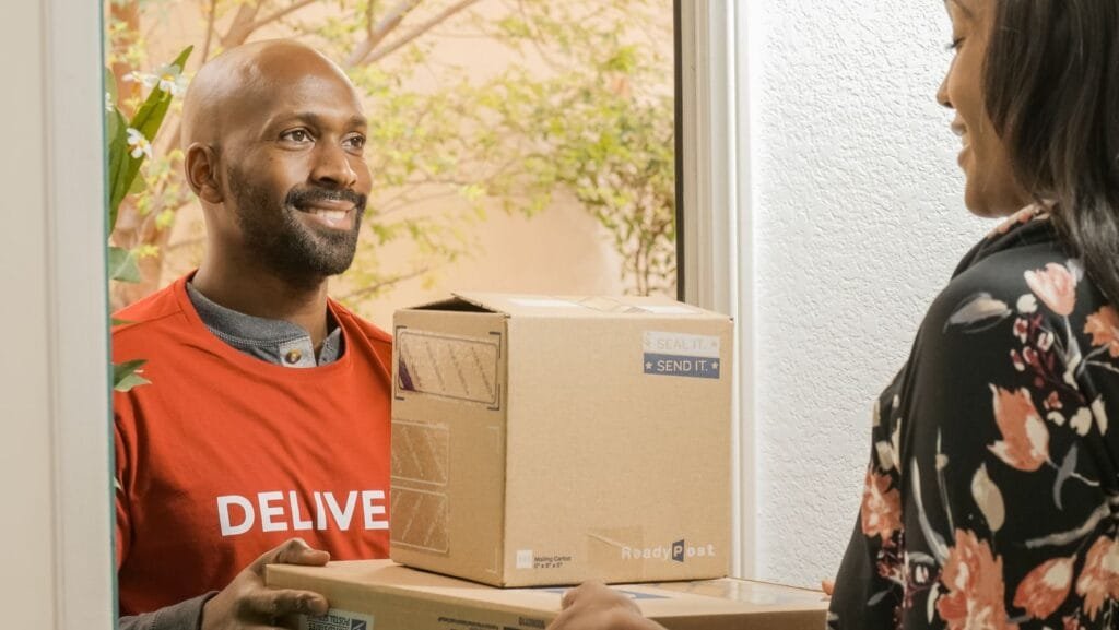 Direitos do consumidor em compras online 1 A delivery person handing packages to a smiling recipient at the door.