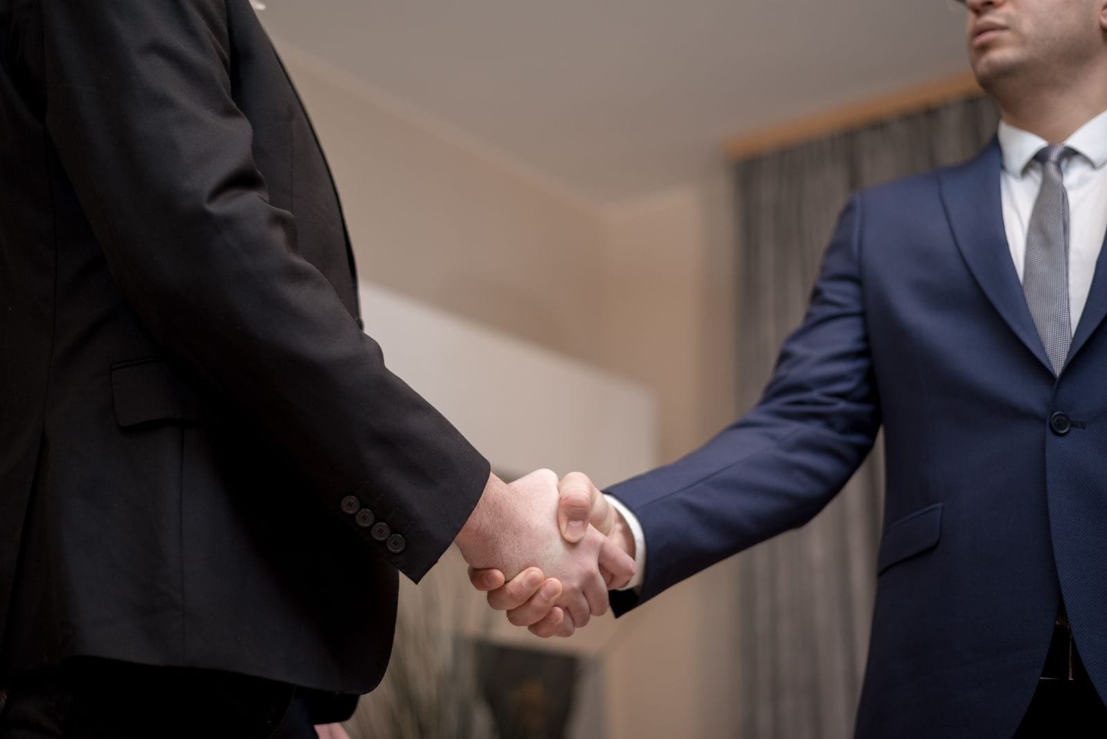 Dissolução de Sociedade: Como Encerrar uma Empresa 1 Two businessmen in suits shaking hands, emphasizing trust and partnership indoors.