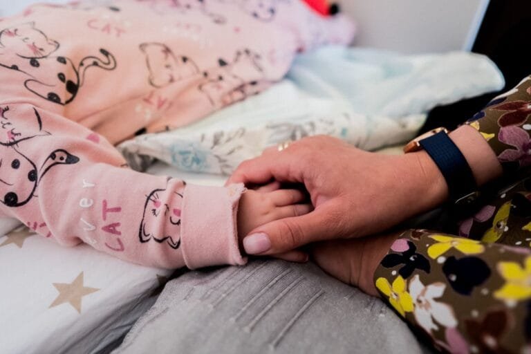 Close-up of mother holding child's hand, depicting warmth and care during bedtime.