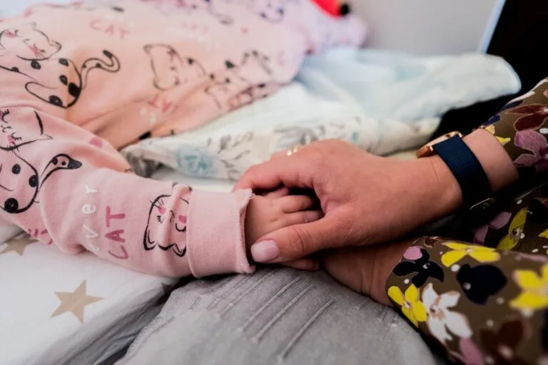 Close-up of mother holding child's hand, depicting warmth and care during bedtime.