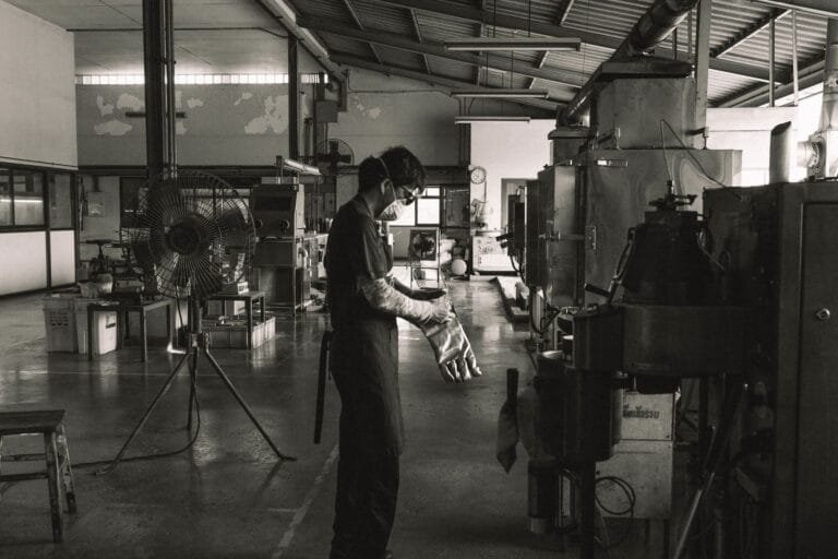 A masked worker operating machinery in a Bangkok factory, showcasing industrial safety.