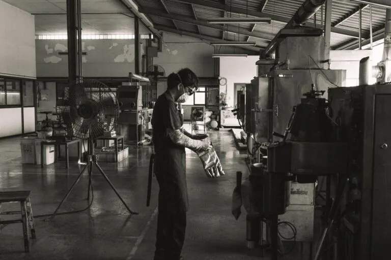 A masked worker operating machinery in a Bangkok factory, showcasing industrial safety.